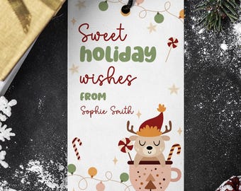 May include: A festive gift tag with the message "Sweet holiday wishes from Sophie Smith" and a deer illustration. The tag is placed near a wrapped gift, a snowflake, and pine cones.