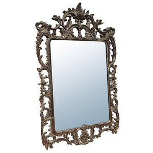 May include: Ornate, rectangular mirror with a decorative, bronze-colored frame. The frame features intricate scrollwork, floral accents, and a detailed top crest. The mirror's surface reflects a light blue hue.