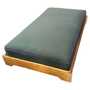 May include: A green upholstered daybed with a bamboo frame. The daybed has a pink trim around the edge of the cushion.