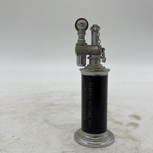 May include: A silver and black vintage lighter with the text "SANDRA MOTORS INC. OF SCOTTSDALE, ARIZONA" on the side.