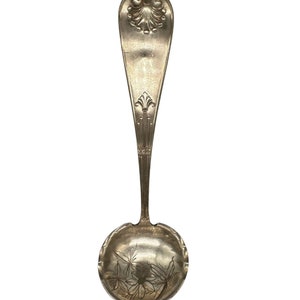 May include: A silver serving spoon with an ornate handle and a round bowl with an engraved floral design.
