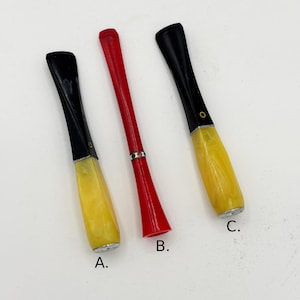 May include: Three vintage cigarette holders. Two have black mouthpieces and yellow bodies, with a gold-colored band. The third is red with a decorative band. All are on a white background.