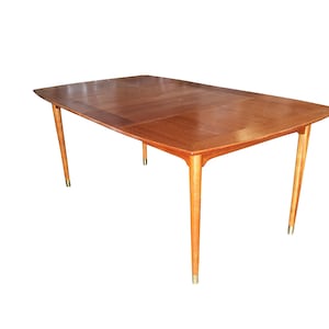 May include: A mid-century modern dining table with a wood top and brass accents. The table has a rectangular shape with rounded corners and a leaf extension.