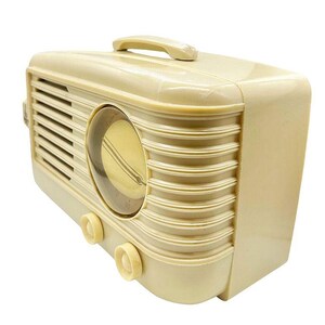 Puede incluir: Radio vintage de color crema con asa en la parte superior. La radio tiene un dise&ntilde;o curvo con l&iacute;neas horizontales y un dial circular. Dos perillas de color crema son visibles en la parte delantera.