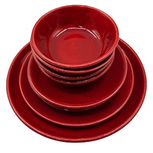 May include: A set of stacked dinnerware featuring a deep red, glossy finish. The collection includes a large dinner plate at the base, followed by a smaller salad plate, and topped with a small, deep bowl. Each piece has a smooth, rounded edge.