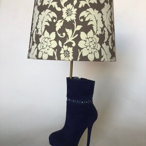 May include: A table lamp with a floral patterned lampshade and a blue suede boot base.