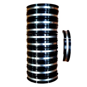 May include: A stack of black and silver bangles. The bangles are stacked in a tower, with the silver band facing outward. There is a single bangle lying on its side to the right of the stack.