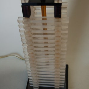 May include: A modern table lamp with a black base and a clear acrylic shade. The shade is made up of stacked, rectangular pieces of acrylic.