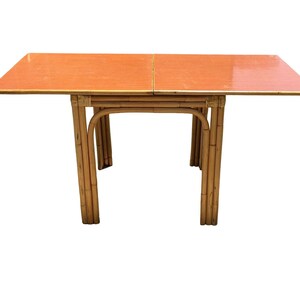 May include: A rectangular, orange-toned table with a bamboo frame. The table has a simple design with four legs and a flat top.