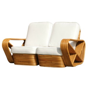 May include: A white two-seater bamboo sofa with curved arms and white cushions.