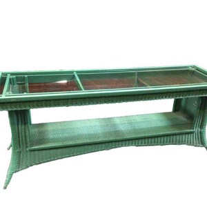 May include: A green wicker coffee table with a glass top and a lower shelf. The table has a unique curved design.