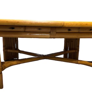 Pode incluir: Uma mesa de centro redonda de madeira com tampo de bambu tran&ccedil;ado e base em forma de cruz.