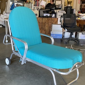 May include: A turquoise blue chaise lounge with a silver frame and wheels. The chaise lounge is made of metal and fabric and has a comfortable, padded seat.