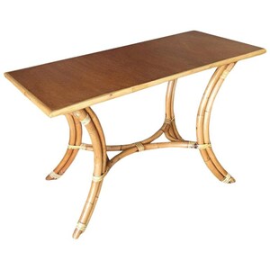 May include: A rectangular, light brown wooden table with a curved, woven bamboo base. The table has a natural wood finish and is supported by four legs.