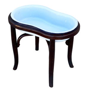 May include: A kidney-shaped basin with a smooth, light blue enamel interior and a dark blue rim, set into a dark brown, curved wooden frame with four slender, arched legs that provide a stable base for the elevated, oval-shaped basin structure.