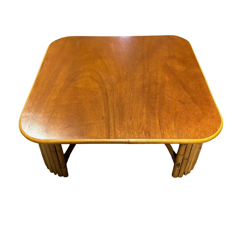 Pode incluir: Uma mesa de centro retangular de madeira com um tampo de cor castanho claro e uma borda arredondada. A mesa &eacute; suportada por uma base de bambu tecido.