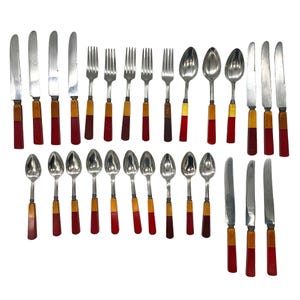 May include: A collection of vintage silverware, including knives, forks, and spoons. The utensils have silver blades and tines, with handles featuring a combination of red, brown, and yellow hues. The arrangement suggests a formal dining setting.