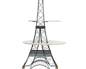 May include: A black metal Eiffel Tower-shaped stand with two round wooden shelves. The stand has four wooden wheels.