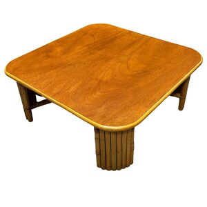 Pode incluir: Uma mesa de centro quadrada feita de bambu natural com tampo de madeira marrom claro. A mesa tem uma borda arredondada e um design simples.