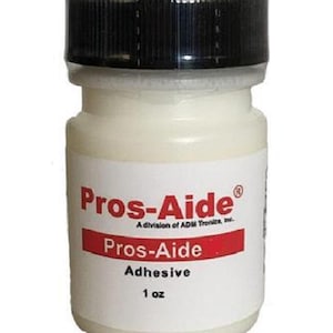 May include: A small, white bottle of Pros-Aide adhesive with a black cap. The label features the brand name in red and white, along with the text "Adhesive" and "1 oz."