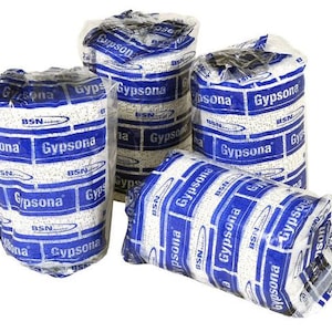 Op de afbeelding: Vier rollen witte gaasverbanden verpakt in blauwe en witte verpakking met de tekst "Gypsona BSN" die op de verpakking wordt herhaald.