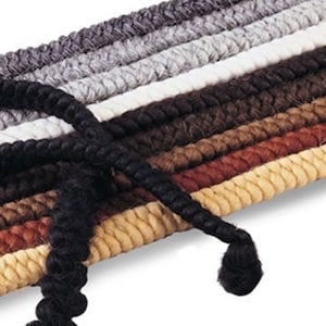 May include: Close-up of a selection of braided rope in various shades of brown, gray, and cream. A length of black rope is in the foreground, with a looped end. The ropes are tightly woven, suggesting a durable material suitable for crafts or home decor.