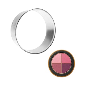 May include: A stainless steel round cookie cutter next to a makeup palette. The palette is round with a black rim and contains four shades of pink and purple eyeshadow.