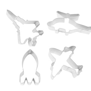 May include: Set of four metal cookie cutters shaped like a rocket, airplane, helicopter, and fighter jet.