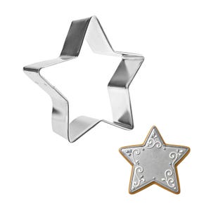 May include: A shiny, silver star-shaped cookie cutter next to a decorated star-shaped cookie. The cookie cutter is made of metal. The cookie has a silver center with white scrollwork and a gold border.