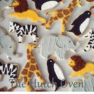 May include: A collection of decorated sugar cookies featuring various animal designs, including a zebra, giraffe, penguin, lion, and elephant. The cookies are decorated with intricate details and bright colors.