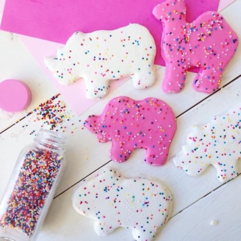 May include: Five pink and white frosted sugar cookies shaped like animals. The cookies are decorated with colorful sprinkles. The cookies are on a white surface.