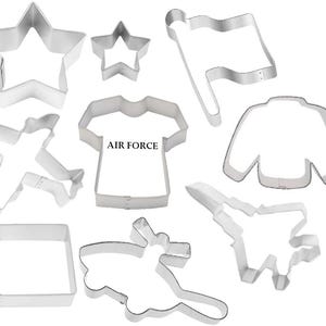 May include: A collection of silver-colored metal cookie cutters in various shapes, including stars, a flag, a shirt with "AIR FORCE" text, a sweater, a square, and airplanes. These cutters are ideal for creating themed treats.