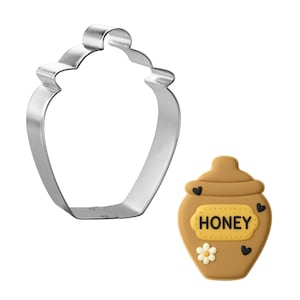 May include: A stainless steel cookie cutter in the shape of a honey pot next to a decorated honey pot cookie. The cookie is brown with a yellow label that says "HONEY". The cookie is decorated with black hearts and a white flower.