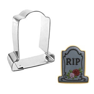 May include: A metal tombstone-shaped cookie cutter next to a decorated cookie. The cookie is gray with the letters "RIP" and a floral design. The cookie cutter is made of shiny, silver-colored metal.