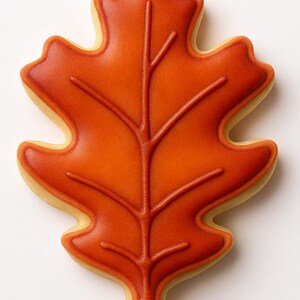 May include: A leaf-shaped cookie with orange icing and a detailed vein design. The cookie has a light-colored edge, and the orange icing is smooth and glossy. This autumn-themed treat is perfect for fall celebrations.