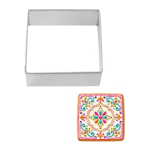 May include: A square cookie cutter made of silver metal sits above a decorated square cookie. The cookie has a white base with a colorful floral design in pink, teal, orange, and yellow. The cookie has a pink border.