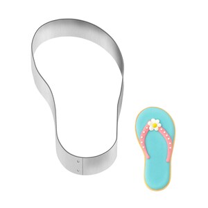 May include: A stainless steel flip-flop shaped cookie cutter next to a decorated flip-flop cookie. The cookie has a light blue base, pink strap with white dots, and a white flower with a yellow center.
