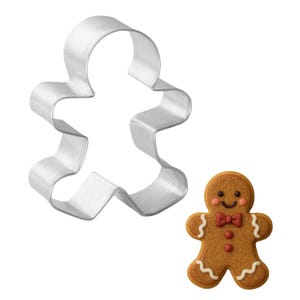 May include: A stainless steel gingerbread man cookie cutter next to a decorated gingerbread cookie. The cookie has a brown base with white icing details, a red bow tie, and a smiling face. Perfect for holiday baking.