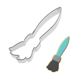 May include: A silver-colored metal cookie cutter in the shape of a paintbrush, next to a decorated cookie. The cookie has a blue handle, gray ferrule, and black bristles, with a gold border.