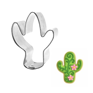 May include: A silver-colored metal cactus-shaped cookie cutter next to a decorated cactus cookie. The cookie is green with pink flowers and decorative icing. The cookie cutter is made of shiny metal.