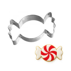 May include: A shiny, silver candy-shaped cookie cutter next to a decorated candy. The candy has a red and white spiral design with white wrapper ends and a gold border. The cookie cutter is made of stainless steel.