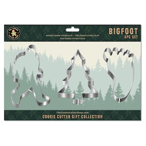May include: A set of three metal cookie cutters shaped like a Bigfoot, a Christmas tree, and a footprint. The cookie cutters are silver and have a shiny finish. The packaging is green and brown with the words "Bigfoot 3PC Set" printed on it.