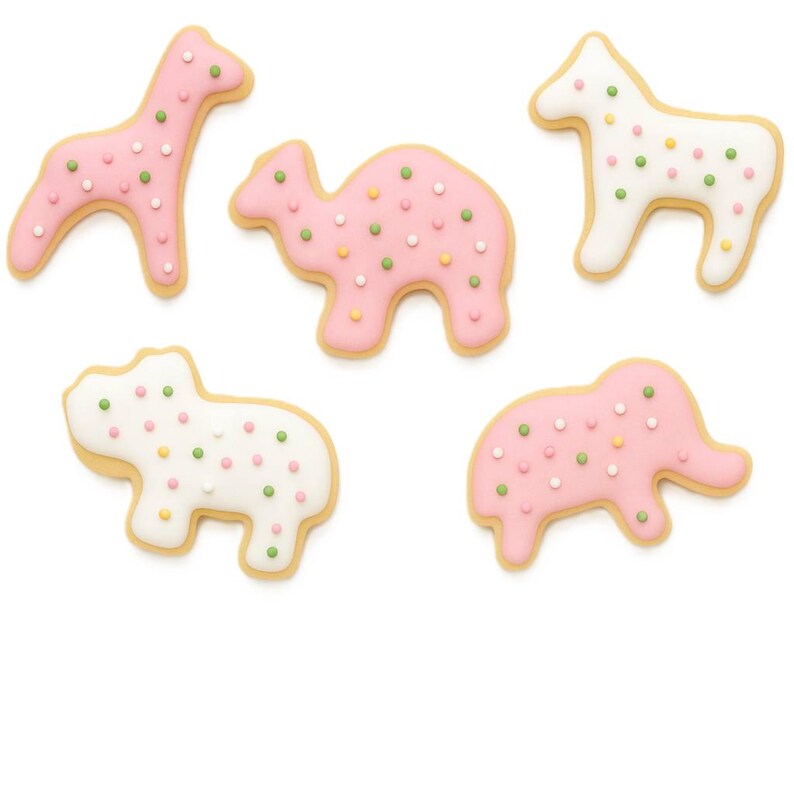 May include: Five animal-shaped cookies with pink and white frosting and colorful sprinkles. The cookies include a giraffe, camel, horse, hippo, and elephant, all with a light brown cookie base.