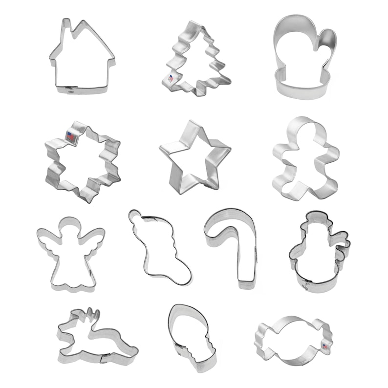 May include: A collection of fourteen silver-colored metal cookie cutters in various holiday shapes, including a house, Christmas tree, mitten, snowflake, star, gingerbread person, angel, stocking, candy cane, snowman, reindeer, light bulb, and candy.