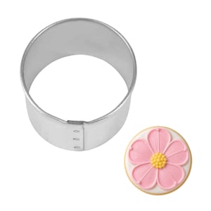 May include: A round, silver-colored cookie cutter next to a decorated sugar cookie. The cookie is round with a pink flower design and a yellow center. The cookie cutter is made of metal.