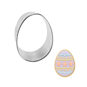 May include: A stainless steel, oval-shaped cookie cutter next to a decorated Easter egg. The egg is light purple with yellow and blue stripes and pink flower details. The cookie cutter is a simple, open circle.