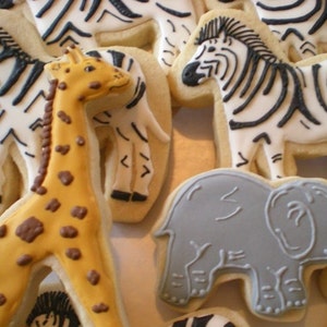 May include: Assortment of animal-shaped sugar cookies decorated with icing. The cookies include a giraffe, zebra, elephant, and rhinoceros.