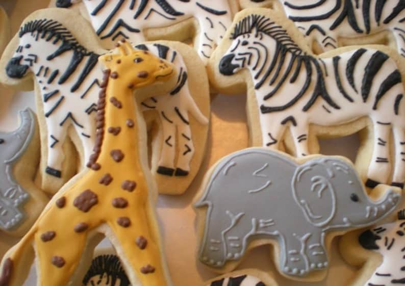 May include: Assortment of animal-shaped sugar cookies decorated with icing. The cookies include a giraffe, zebra, elephant, and rhinoceros.