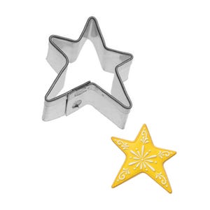 May include: A stainless steel star-shaped cookie cutter next to a yellow star-shaped cookie with white decorative icing. The cookie cutter is made of shiny metal and has a simple, five-pointed star shape. The cookie is decorated with intricate white icing.