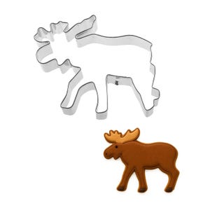 May include: A stainless steel moose-shaped cookie cutter and a decorated moose-shaped cookie. The cookie cutter is a simple outline of a moose. The cookie is brown with a lighter brown antler.